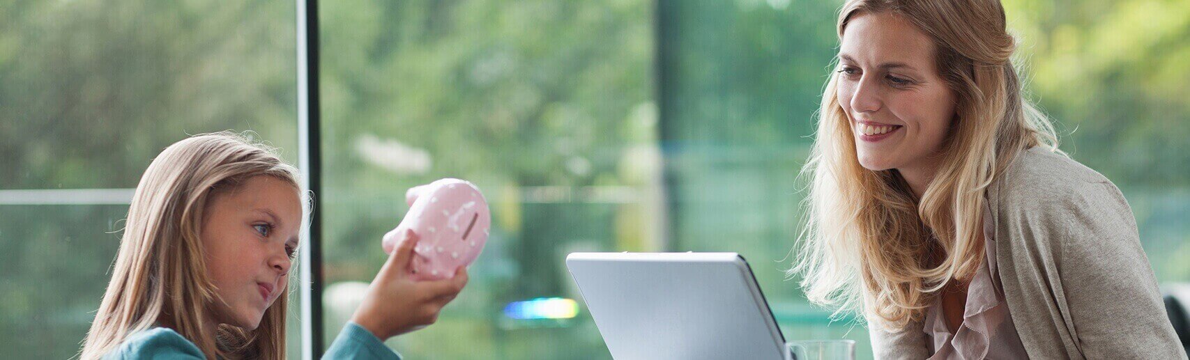 Mother watching her daughter play with a pink piggybank