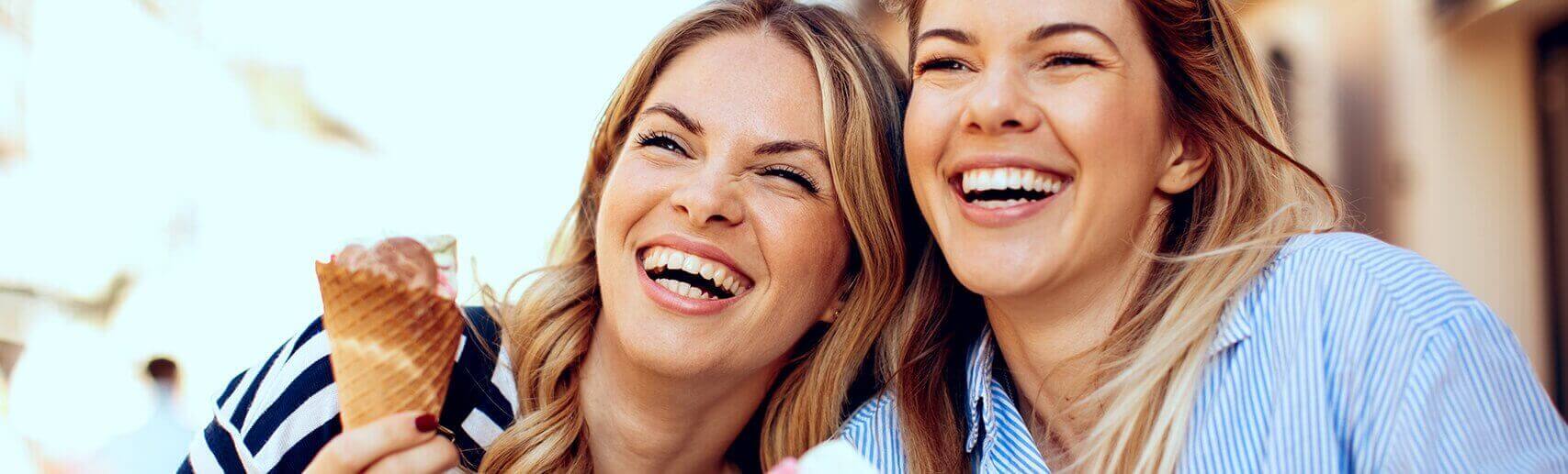 Two blonde women laughing holding an ice cream cone