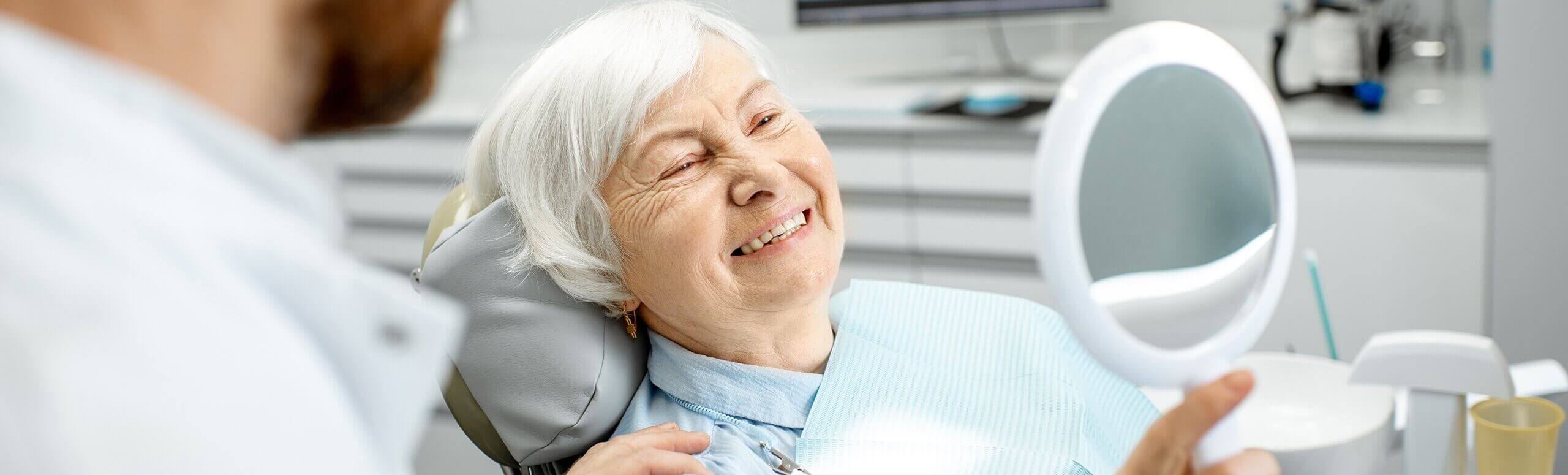 older woman at dentist smiling into a mirror