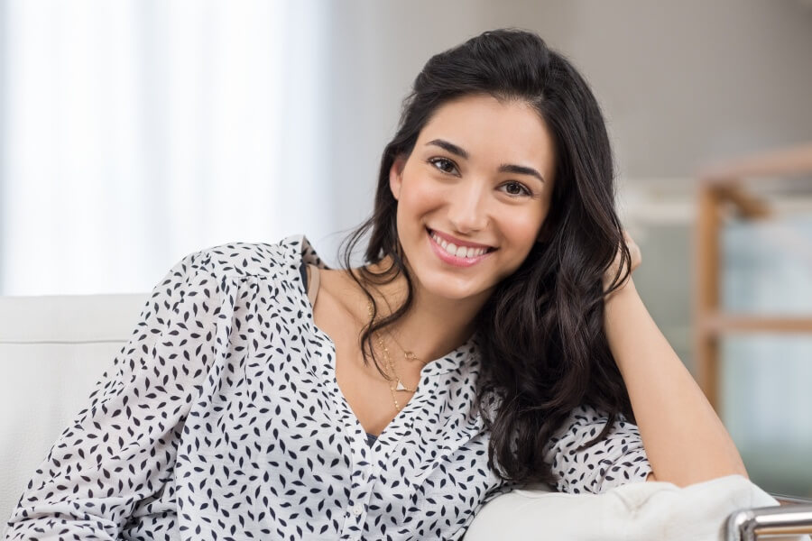 Brunette woman with veneers smiles while leaning on her elbow