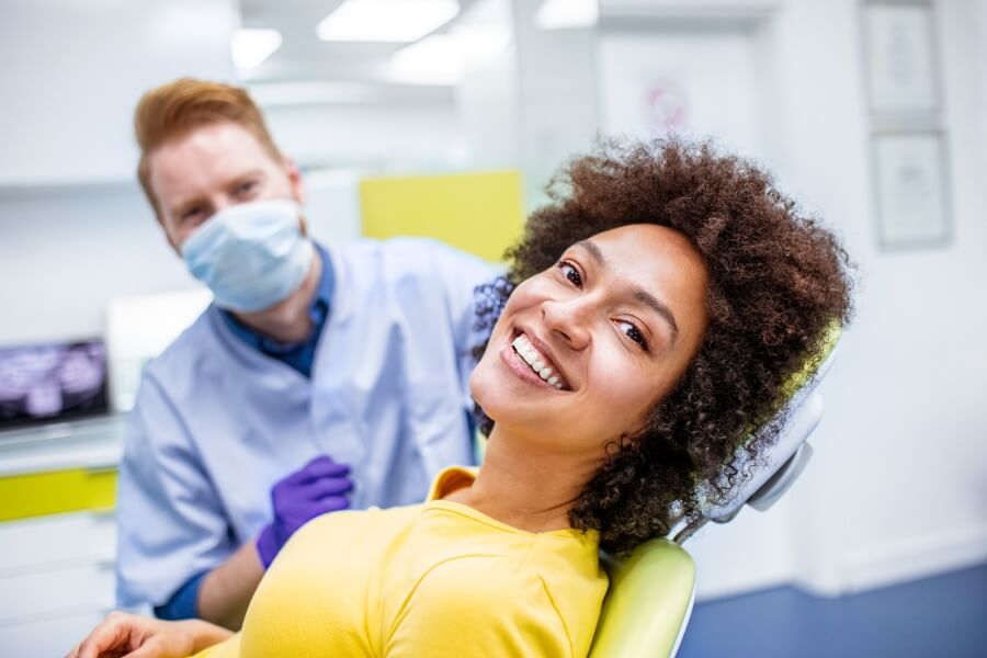 Curly-haired woman in a yellow shirt smiles while sitting in a dental chair in Portland, OR