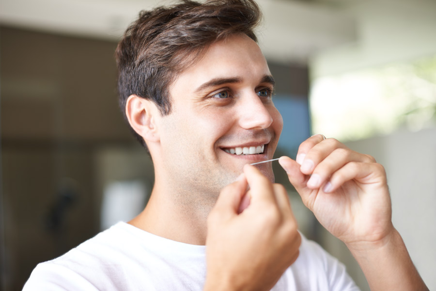 Brunette man smiles as he flosses because he understands it is important for his oral health