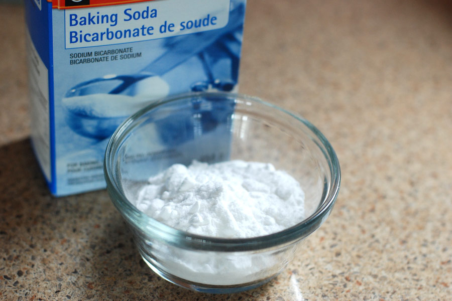 A blue package of baking soda next to baking soda in a clear dish, an ingredient in some toothpaste