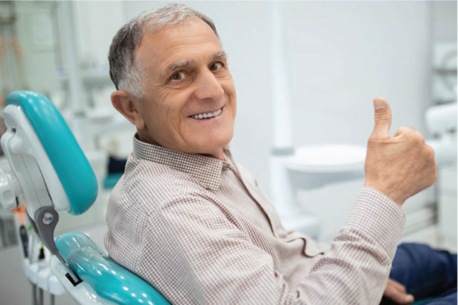 senior man gives a thumbs up after getting fitted for dentures at the dentist
