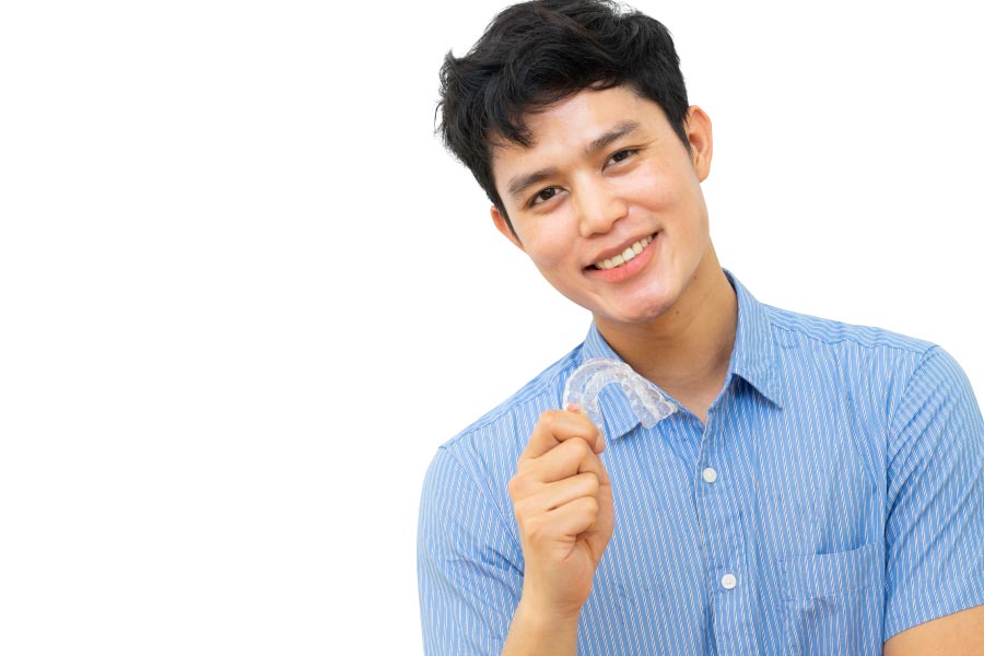 young man smiles and holds up his clear aligner