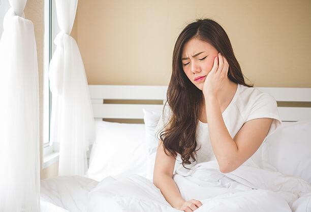 woman sitting up in bed, holding her jaw in pain