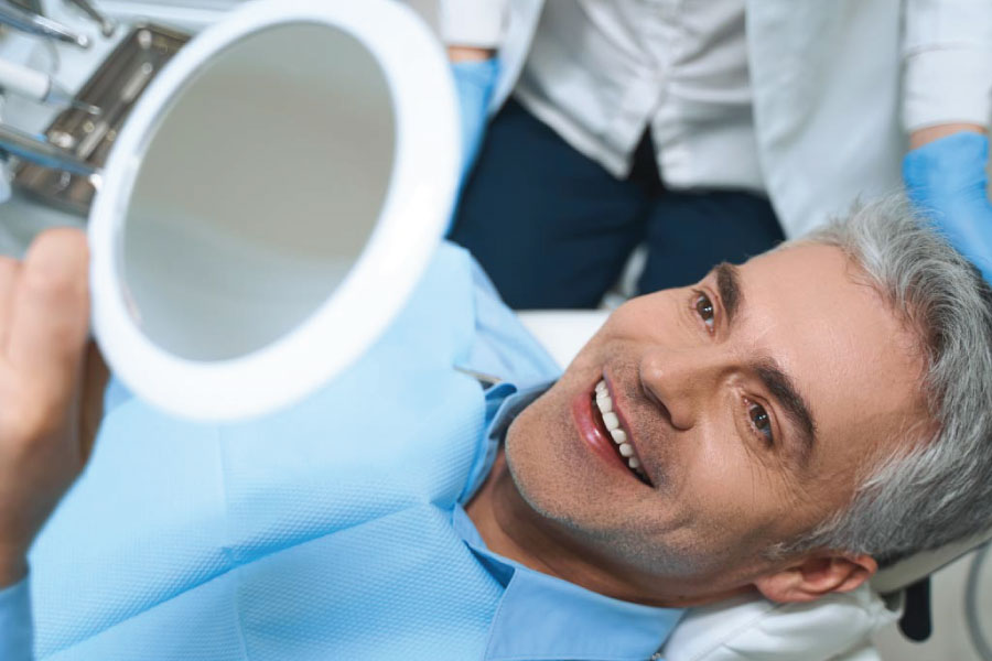 man in the dentist chair looks in a handheld mirror and at his new dental sealants